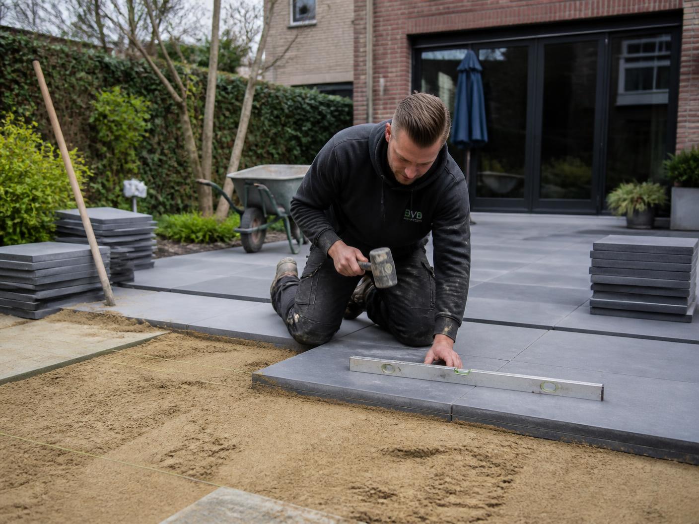 Hovenier legt grote grijze terrastegels waterpas in een moderne achtertuin