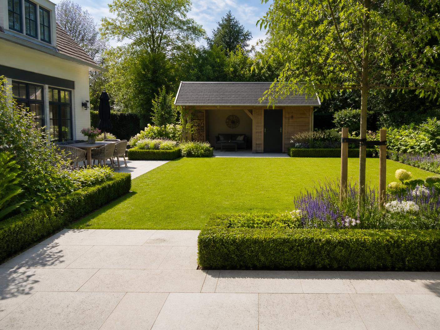 Ruime familietuin met strak gazon, lichte natuurstenen terras, lage hagen en houten tuinhuis